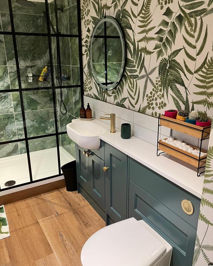 Leafy wallpaper and green cabinetry in bathroom from @janeyeversinteriors with natural and warm accents for green bathroom decor ideas