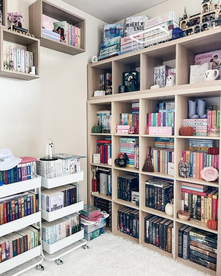 Light wood Ikea Kallax bookshelf styled with colorful books and cozy home decor from @jackyinreadingland. Warm personal touches included.