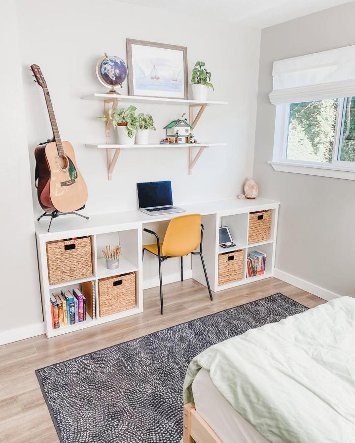 White Ikea Kallax shelf unit styled as a multifunctional workspace with woven baskets, floating shelves, and a yellow chair by @rachelrainbolt. Simple and bright.