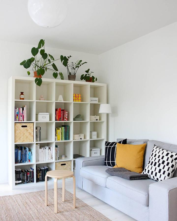 White Ikea Kallax bookshelf with colorful books, neutral baskets, and green plants styled by @annaluopa in bright living room space. ikea kallax bookshelf styling ideas