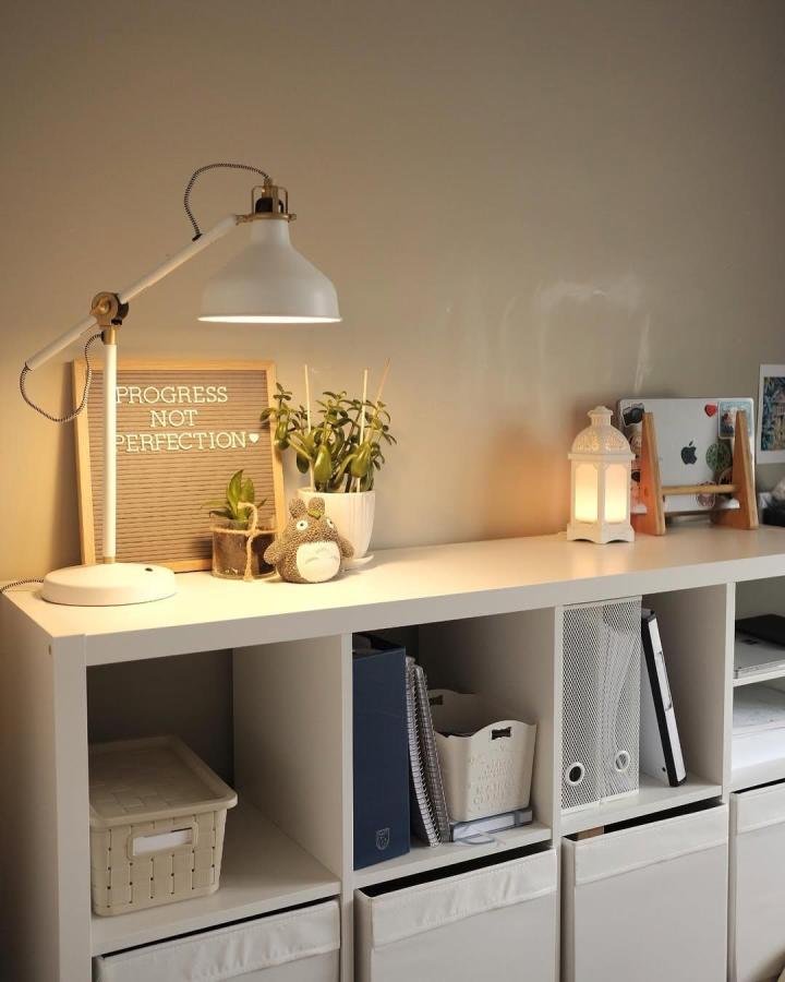 White minimalist Ikea Kallax bookshelf styled with plants, lamp, baskets, and neutral decor by @inhinyero.nina creating cozy vibe.