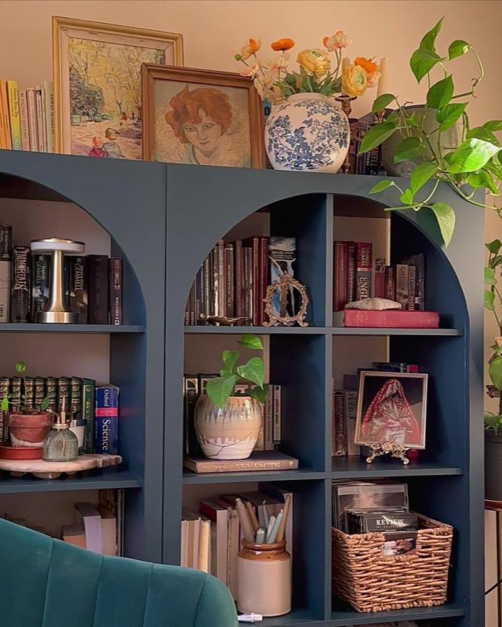 Deep blue ikea kallax bookshelf styling ideas with curved arches, plants, vintage ceramics, and framed art by @handmadehome_durham.
