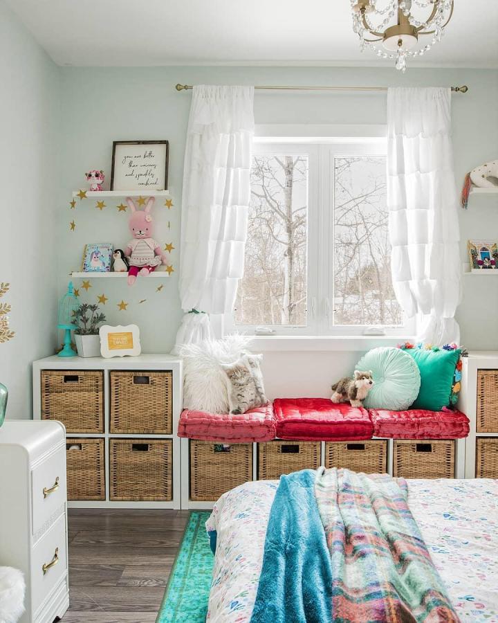 Natural woven basket Kallax shelving unit styled as window seat with red cushions and playful decor from @cozydiyhome ikea kallax bookshelf styling ideas