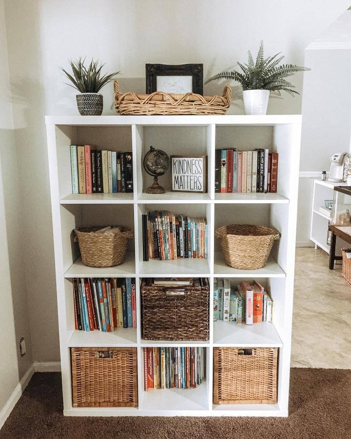 White Ikea Kallax bookshelf with woven baskets, books, and plants styled by @laurenmarieneal showing ikea kallax bookshelf styling ideas with natural textures and cozy colors