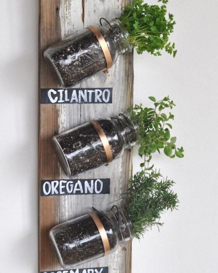 Three glass mason jars filled with soil and fresh herbs mounted on a weathered wooden board with copper bands and chalkboard labels by Rachel Hollis mason jar crafts for adults.