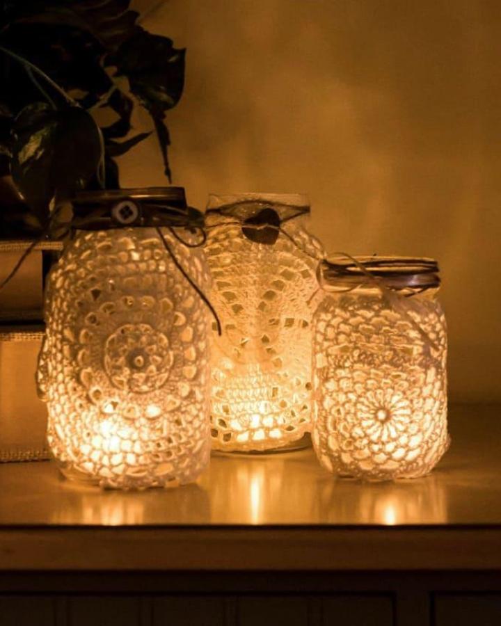 Delicate lace doily covered mason jar luminaries from Crafts by Amanda glowing softly on wooden surface rustic style mason jar crafts for adults.