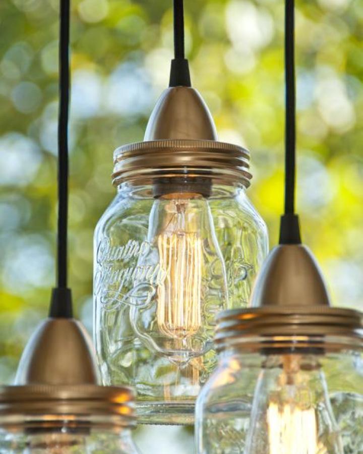 Clear glass mason jar pendant lights with metal lids from MMDIY glowing with vintage Edison bulbs in natural light background.