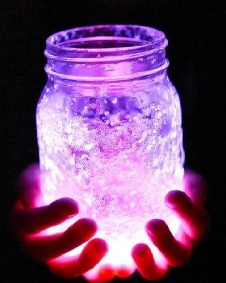 Glowing purple and pink bubble-textured Mason jar crafts for adults from One Little Project held in hands with lights inside shining bright.