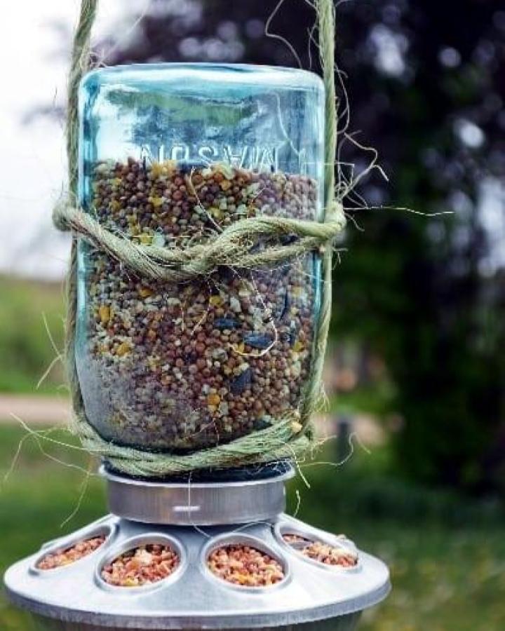 Blue-tinted Mason jar bird feeder from Little House Living with natural twine and metal feeding base outdoors. Rustic mason jar crafts for adults.