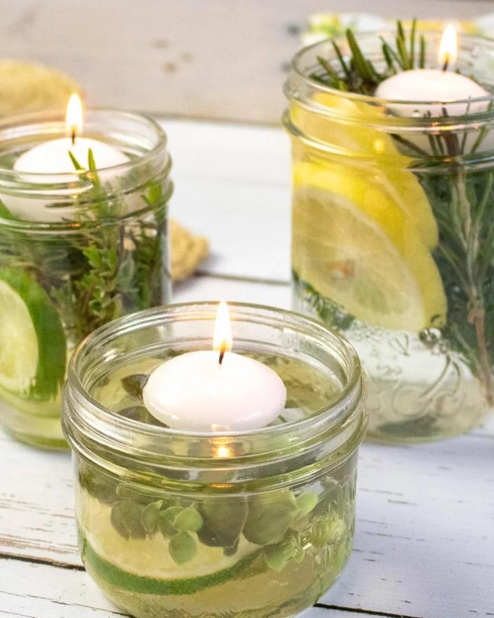 Clear glass mason jars with floating white candles, fresh green herbs, and citrus slices from Crafts by Amanda. Natural, cozy, handcrafted floating candle jars for adults.