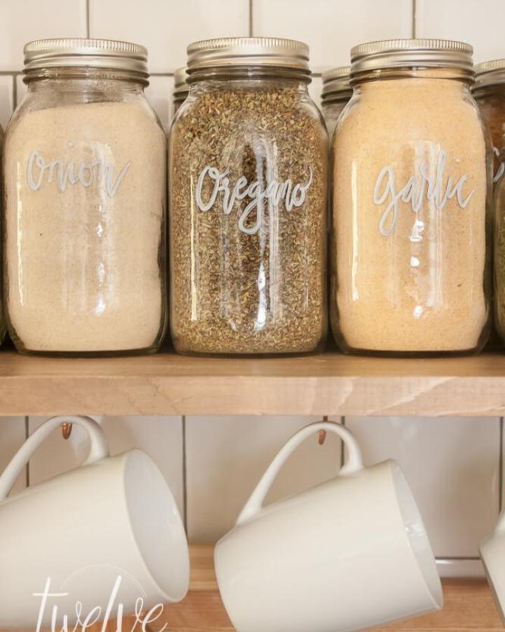 Clear glass Mason jar spice storage with silver lids and white hand-lettered labels on wooden shelf mason jar crafts for adults organization idea.