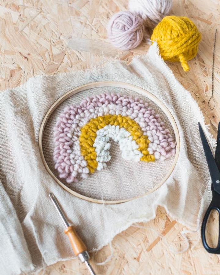 Chunky wool yarn rainbow punch needle craft from fallfordiy for mindful crafts for beginners showing soft pastel and yellow colors in embroidery hoop.