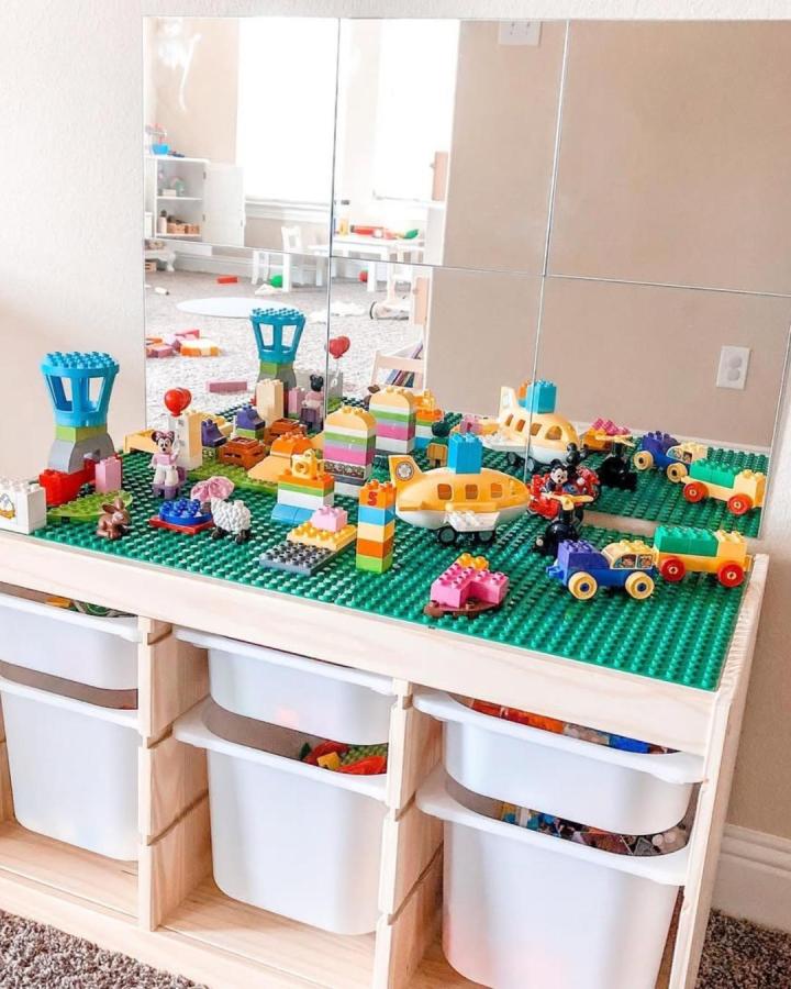 Green Lego baseplate play surface on natural wood Ikea TROFAST with white storage bins from @coffeeandspitup. Organized toy storage with built-in play area.