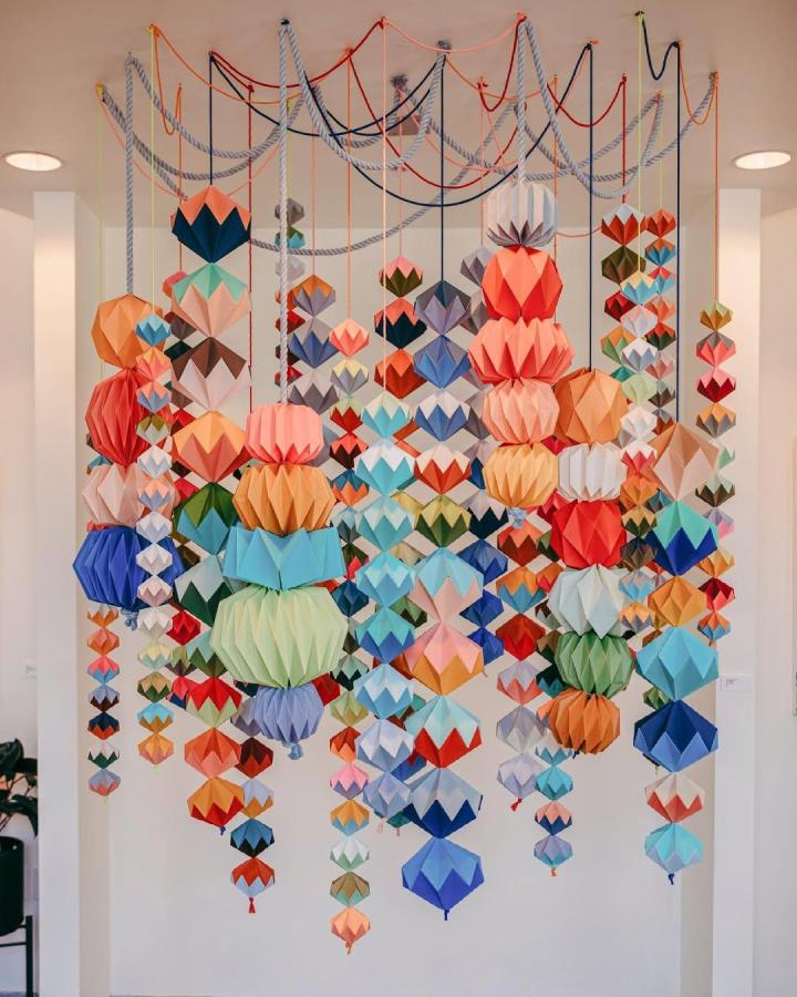 Colorful multi-layered origami lanterns hanging in a modern room from @thepapercommittee. Paper crafts for adults with vibrant geometric shapes.