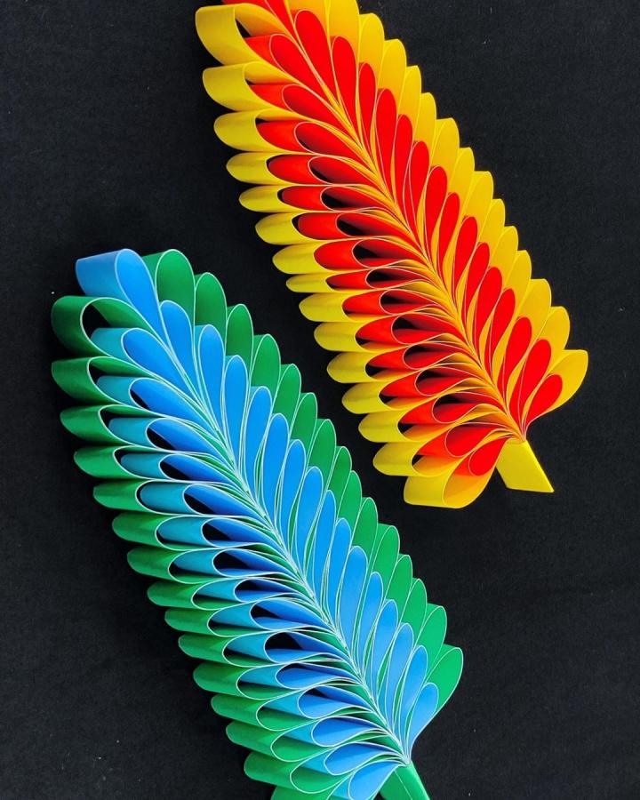 Bright layered paper leaves in green-blue and yellow-red from DIY And Paper Crafts showing detailed folded strips for paper crafts for adults. Vibrant and textured design on black background.