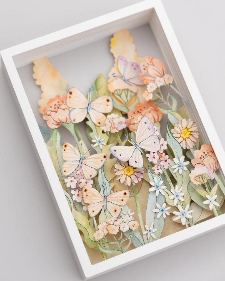 Soft pastel layered butterflies and flowers paper art in a white shadow box frame by @marinapapercuts. Intricate paper crafts for adults with delicate details and gentle colors.
