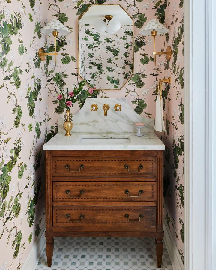 Pink floral wallpaper with green vines in a small powder room by @kerripilchikdesign featuring brass fixtures and marble countertop. Small powder room wallpaper ideas.