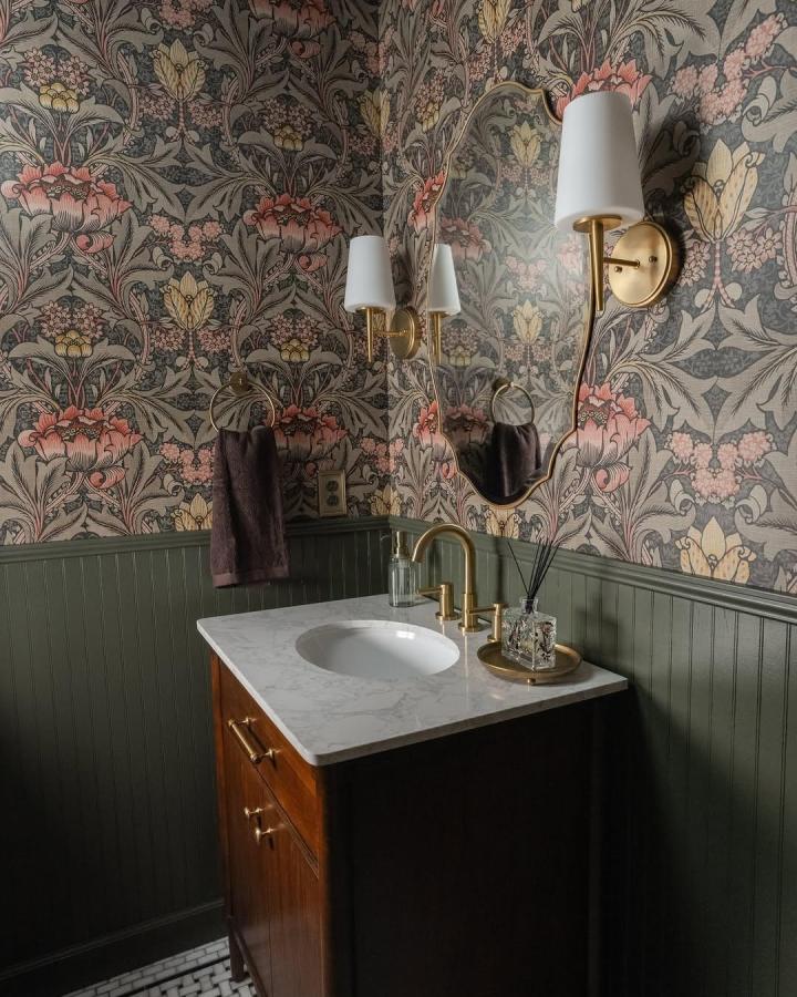 Muted floral vintage wallpaper and olive beadboard in small powder room by @caroldemaurohome. Classic brass details enhance cozy style.