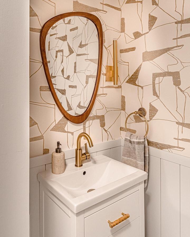 Small cream and gold abstract wallpaper with brass fixtures and wood mirror in small powder room by @amastudiointeriors. Elegant and cozy small powder room wallpaper ideas.