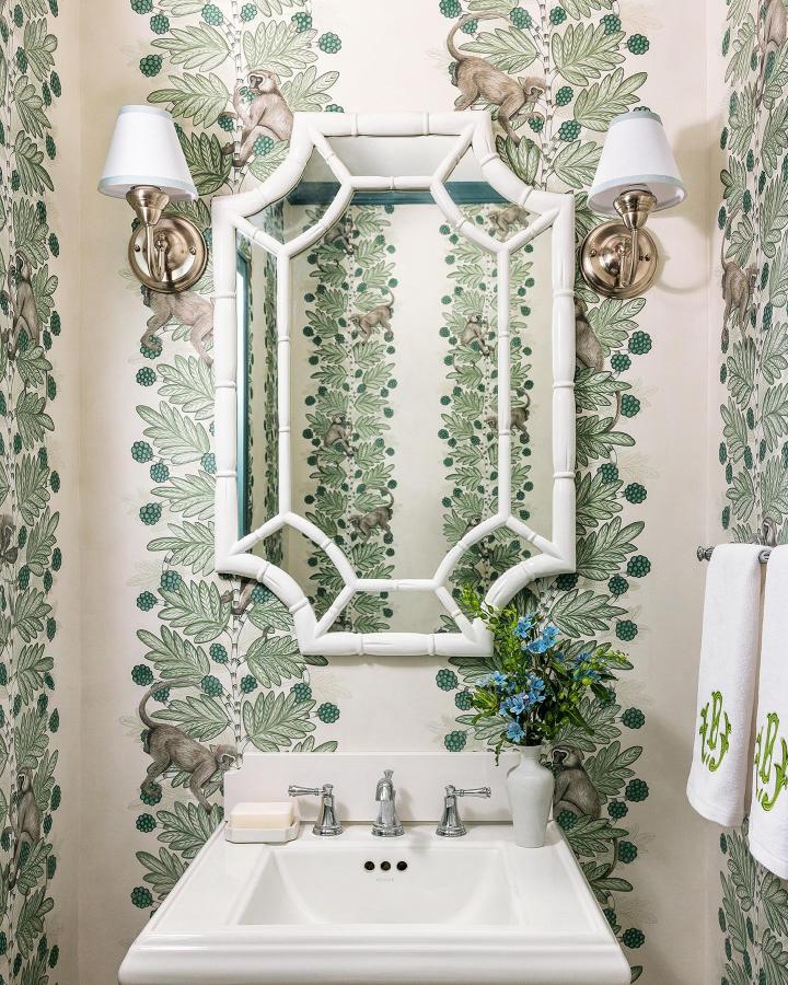 Green leafy and monkey-themed wallpaper in a small powder room with white bamboo mirror from @mollybrunointeriors. Classic elegant small powder room wallpaper ideas.