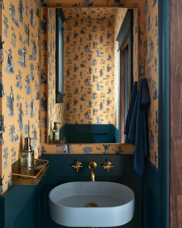 Ochre and deep teal two-tone wallpaper and wood paneling in a small powder room from @divinesavages featuring vintage silhouette motifs and brass fixtures.