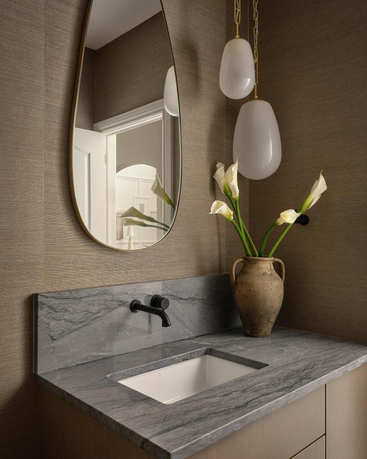 Soft taupe textured wallpaper and gray marble countertop in small powder room from @levdesignbuild with vintage vase and black fixtures.