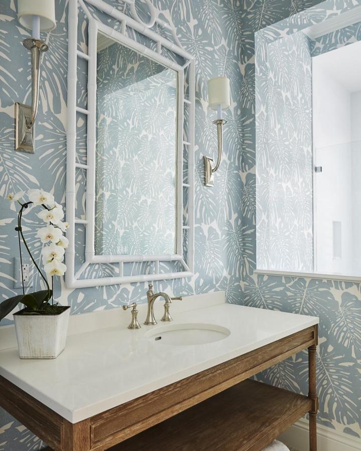 Soft pale blue and white tropical leaf wallpaper in a small powder room from phillipjeffries with natural wood vanity and white framed mirror.