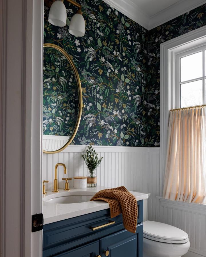 Deep navy floral wallpaper and white beadboard in a small powder room by @madisonnicoledesign with gold fixtures and round mirror small powder room wallpaper ideas.