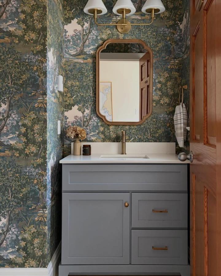 Vintage botanical wallpaper in green and gold tones in a small powder room by @homeonthebayinteriors with grey vanity and brass details.