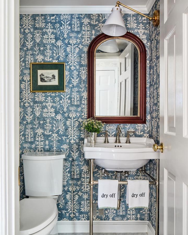 Blue botanical patterned wallpaper in a small powder room by @annepulliaminteriors featuring white fixtures and brass accents creating a charming, cozy look.
