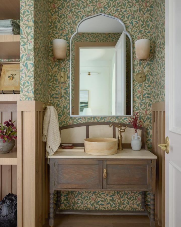 Soft green and red vintage floral wallpaper small powder room with wooden vanity and brass fixtures from @homesbysorensen creating cozy charm.