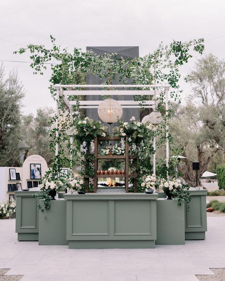 sage green cabinetry and lush greenery wedding bar ideas from Style Me Pretty with white pergola frame and hanging globe lights outdoors elegant floral decor