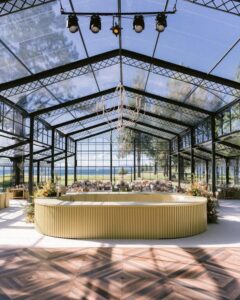 Beige ribbed circular bar in a glasshouse from @hensleyeventresources with natural light and floral accents for wedding bar ideas