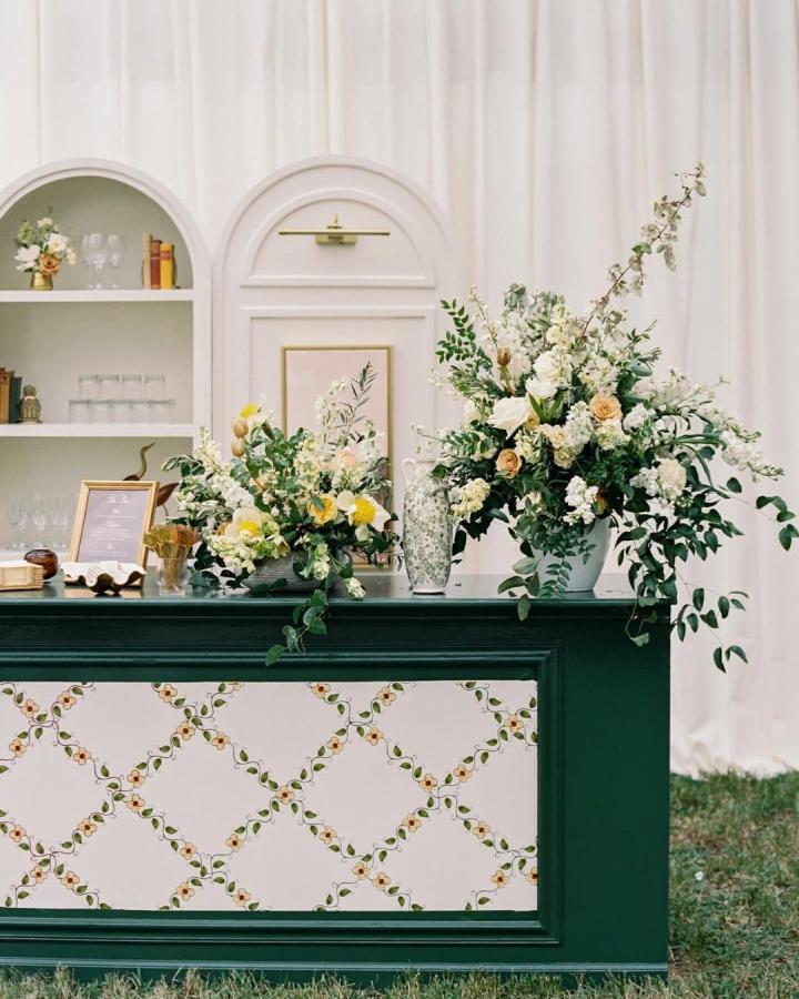 Deep green wooden bar with floral trellis panels and lush white and peach flower arrangements from @browneandtowers wedding bar ideas.