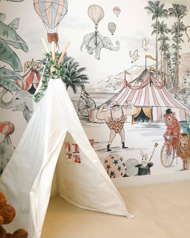 Creamy white teepee and pastel circus wall mural from @annet_weelink_design featuring whimsical characters in a nursery setting. circus nursery ideas