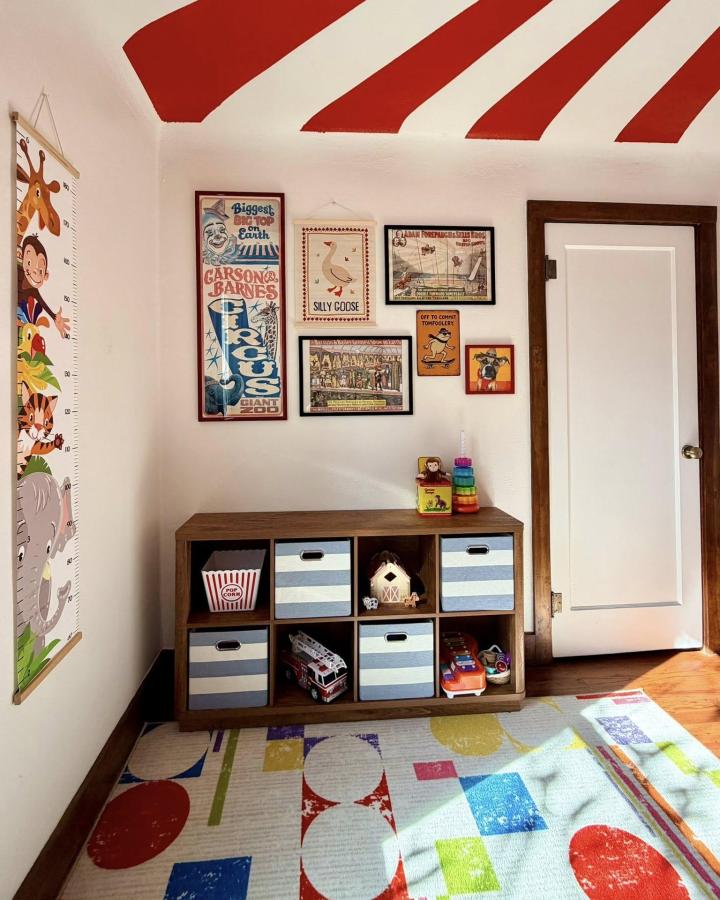 Bright red striped ceiling and vintage circus posters in a cozy nursery by Carli Steiner. Whimsical circus nursery ideas.