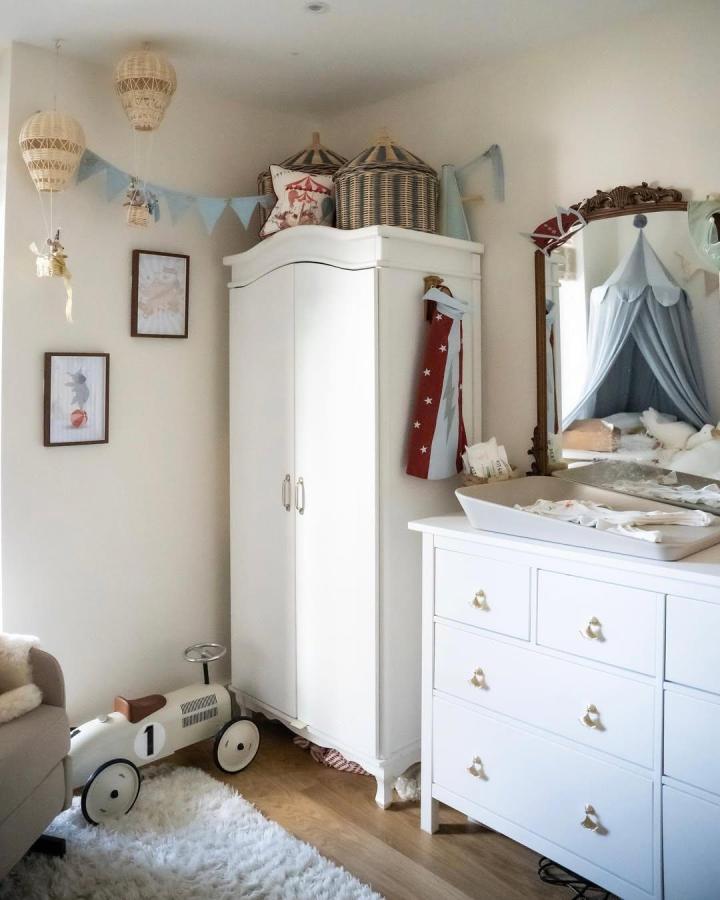 White wardrobe and dresser with wicker baskets from @alexandratealeaf styled with soft blues and vintage circus nursery ideas accents in a cozy nursery corner.