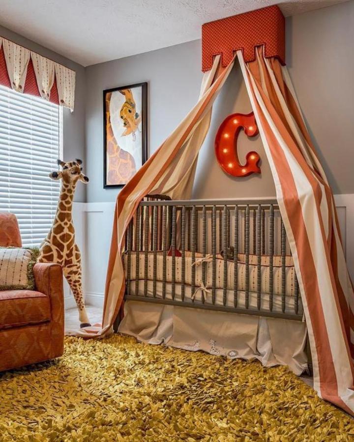 Striped vintage style canopy over crib with light-up letter C and giraffe plush from @candace.decoratingden circus nursery ideas. Cozy and playful.