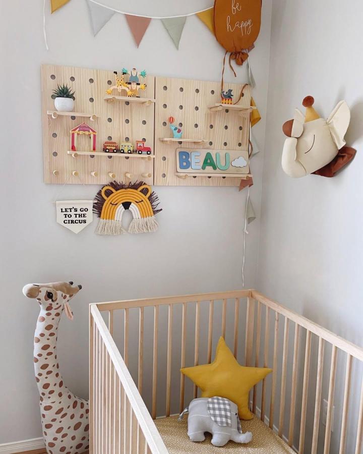 Natural pine pegboard shelves and soft circus-themed toys in a light nursery from @ourhomewithkids. Playful yet calm design.