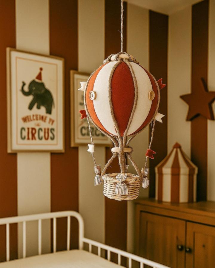 Warm brown and creamy white striped nursery with felt hot air balloon mobile from @lollipouf hanging above crib, circus nursery ideas ambiance.