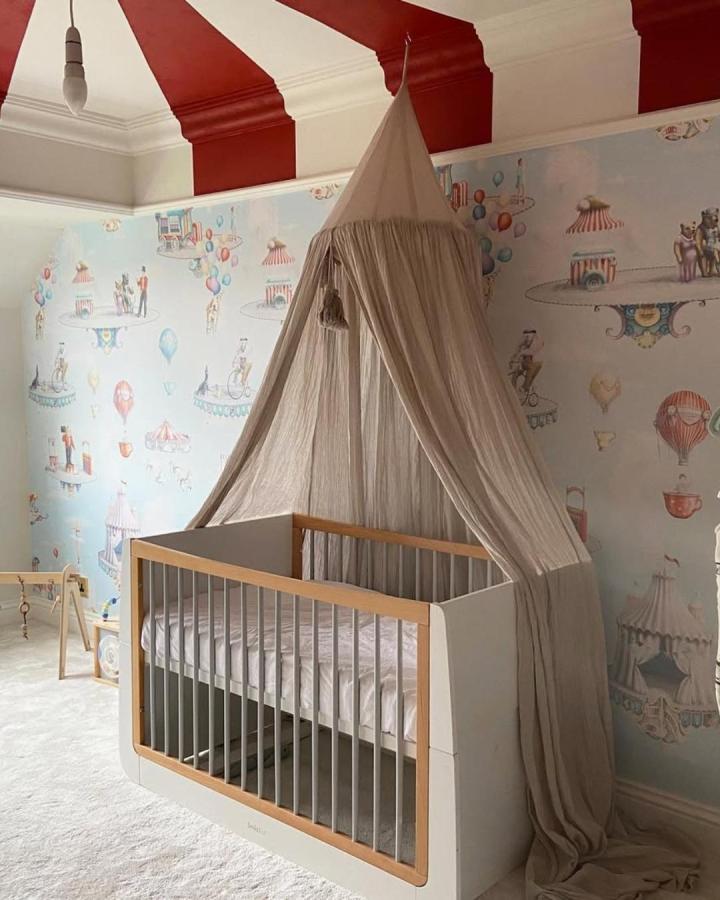 neutral linen canopy tent over modern crib with bold circus wallpaper and striped ceiling from @toddlerintow_reno circus nursery ideas whimsical and cozy ambiance