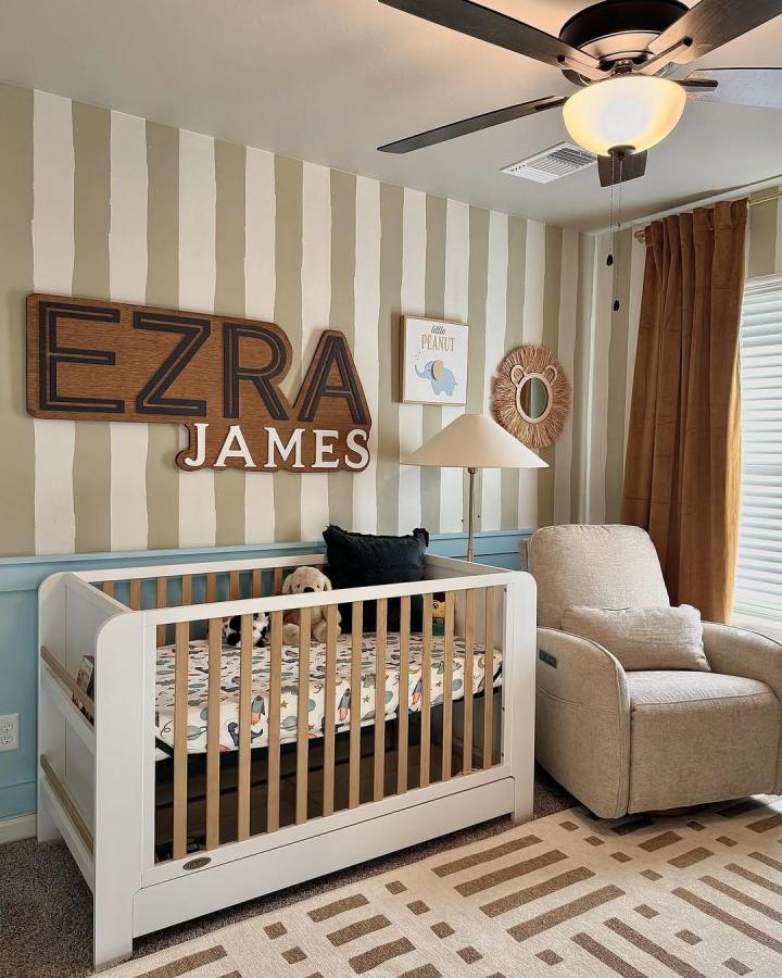 warm wooden personalized name sign nursery wall from @rockymountaindecals with striped wallpaper and cozy beige accents circus nursery ideas