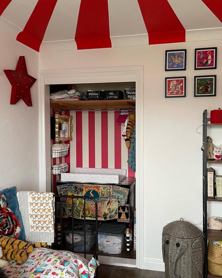 Bright red and white striped circus nursery closet backdrop with vintage posters from @diamondsandfoes. Classic circus nursery ideas flair.