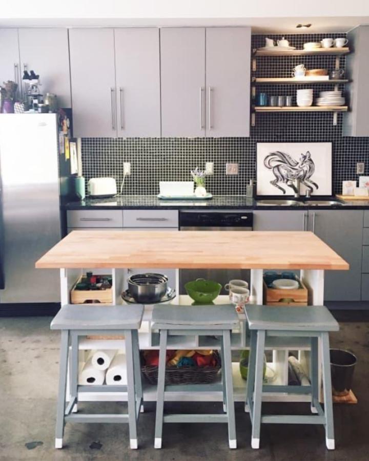 Light wooden top kitchen island with grey stools and open shelf storage in modern kitchen by @el_massey. Practical and stylish seating and storage combo.