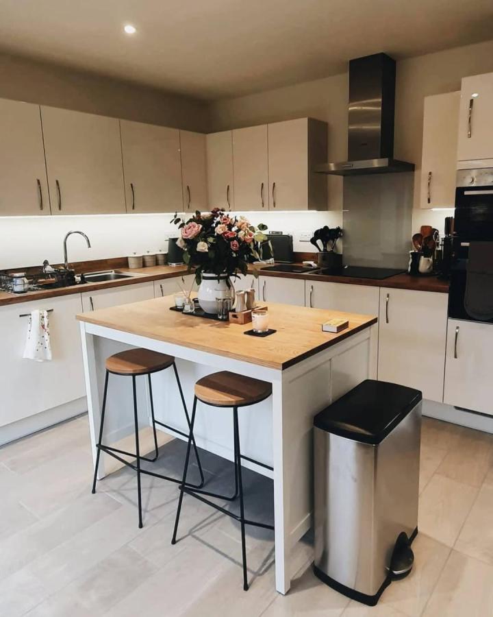 Light wood topped kitchen island with black metal stools and white base by @thehallam_. Cozy modern kitchen with minimalist design and warm accents.