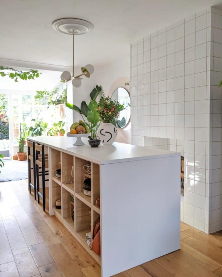 White kitchen island with natural wood open shelves from @two.men.and.the.city. Bright, airy design with modern rustic style and practical storage.