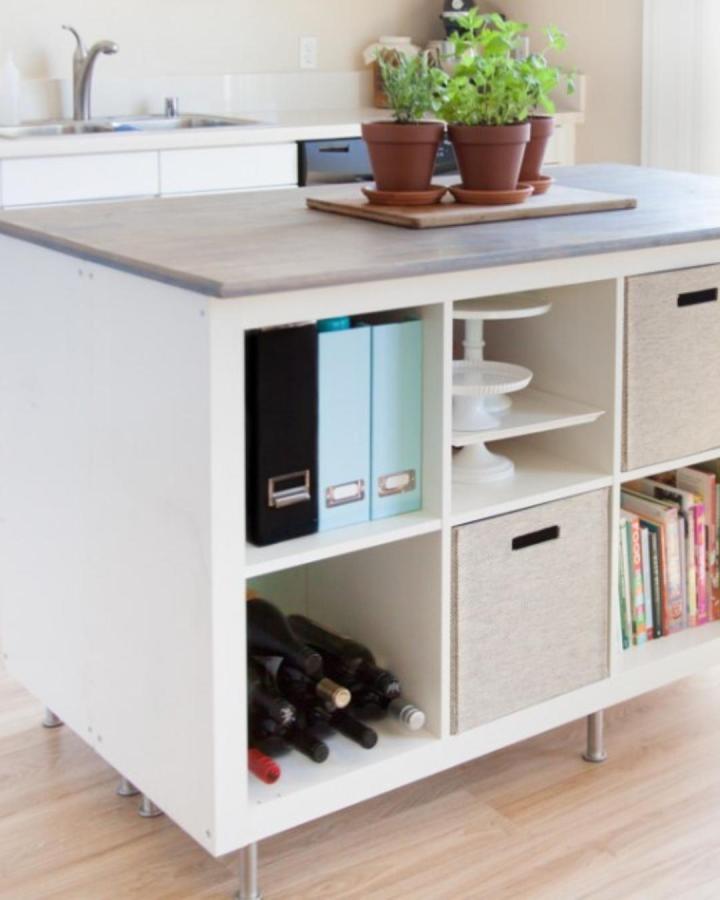 White kitchen island with open storage cubes and fabric bins from DIY Kitchen Island. Features wood top, metal legs, and organized compartments.