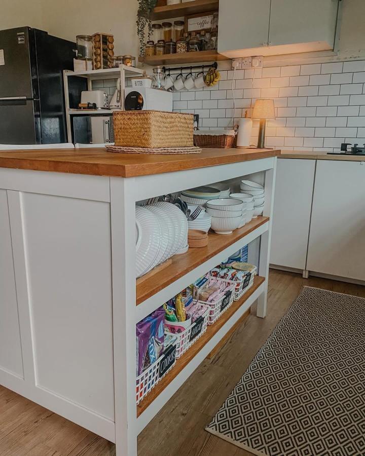 White kitchen island with wood shelves and baskets showing organized dishes and snacks ikea kitchen island hacks by @homey.farmhouse.