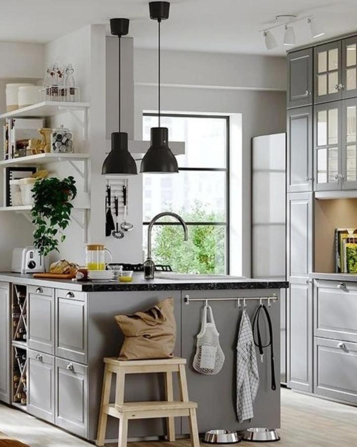 Gray paneled kitchen island with black countertop, open wine rack, hanging rails, and wooden step stool in bright kitchen by @ikea_kitchen_design.
