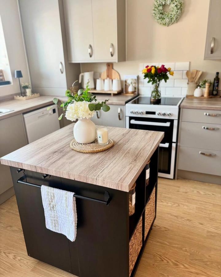Black kitchen island with wood countertop and wicker baskets storage from @sjw.home. Featuring towel rail and natural minimalist styling.